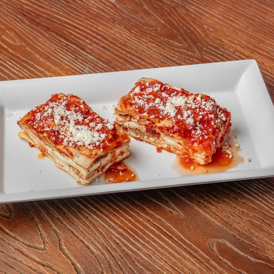 Two slices of Little Lorenzo's Italian Deli & Catering lasagna with red sauce and cheese on a white plate.