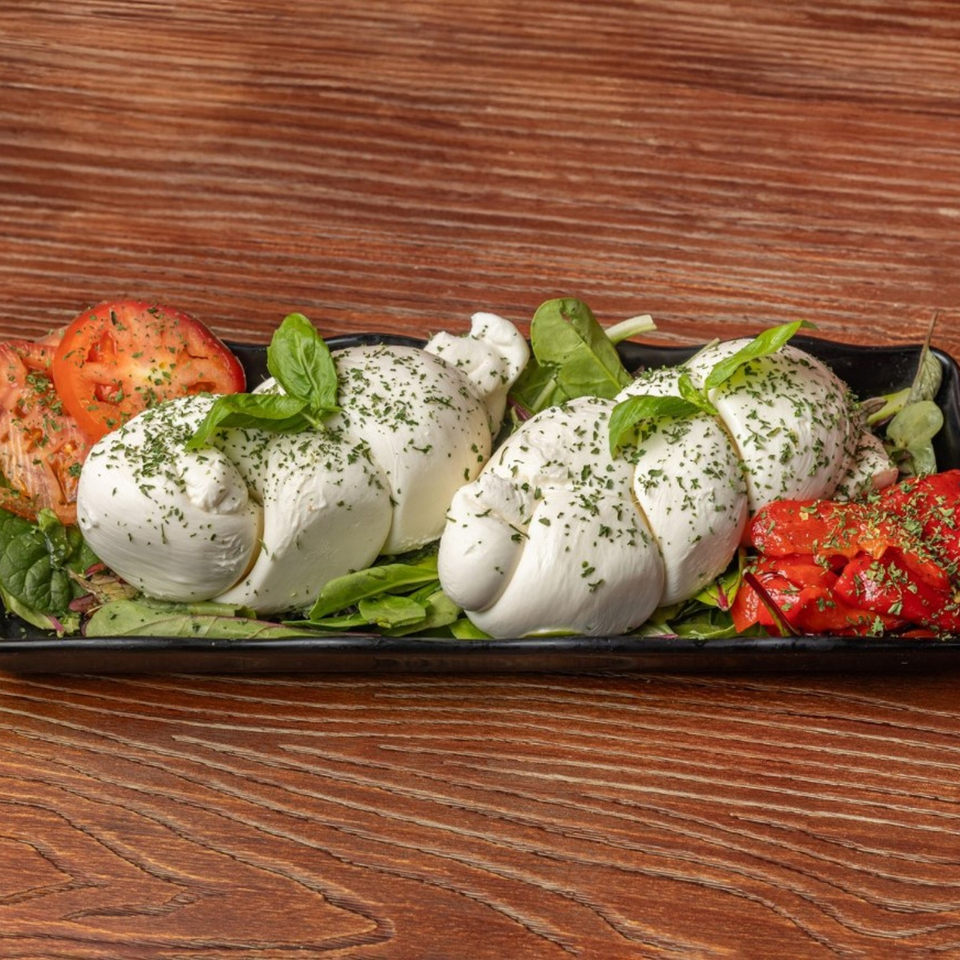 Fresh mozzarella balls with basil, sliced tomatoes, and roasted red peppers on a black platter.